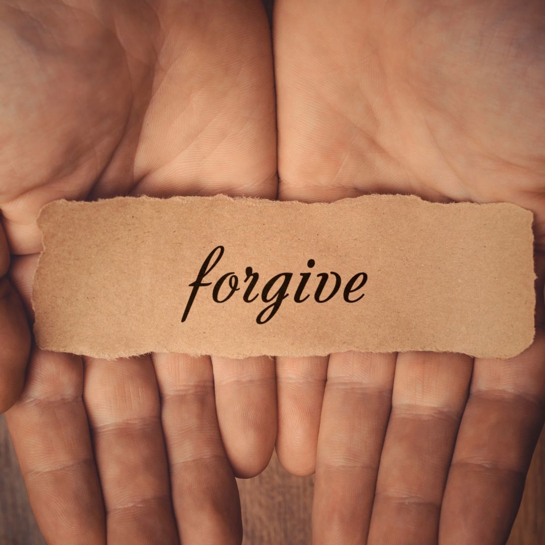 dłonie z kartką z napisem forgive funadamenty radykalnego wybaczania